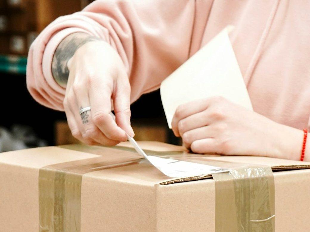 Mãos colando a etiqueta de envio numa caixa de papelão.