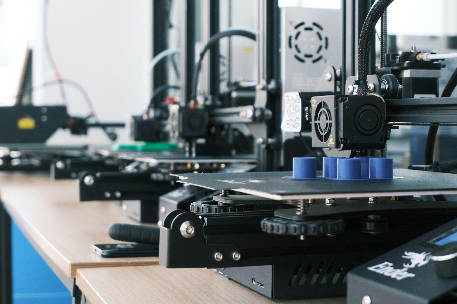 Fileira de impressoras 3D imprimindo peças azuis numa bancada de madeira.